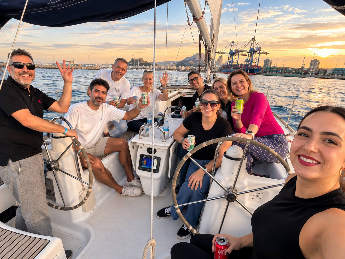 Participantes reunidos en la bañera de un velero frente al puerto de Alicante al atardecer